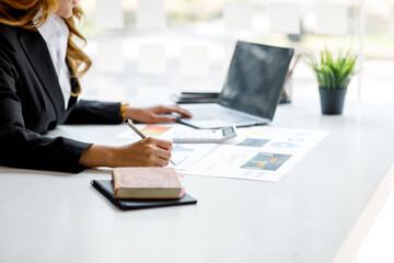 Asian Businesswoman sitting on laptop computer planning accounting analyze report investment and marketing on the desk in the office.