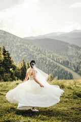 Fototapeta na wymiar A beautiful bride in a white dress is spinning in the mountains.