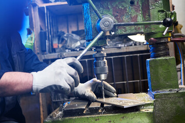 Employee drilling aluminium flat steel plate with bench drill. Metal Drill bit makes holes in Steel billet on industrial machine. Metal work industry