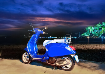 Blue Motor bike at Patong Beach Phuket Thailand at night. Lush green trees in the background white sandy beach.