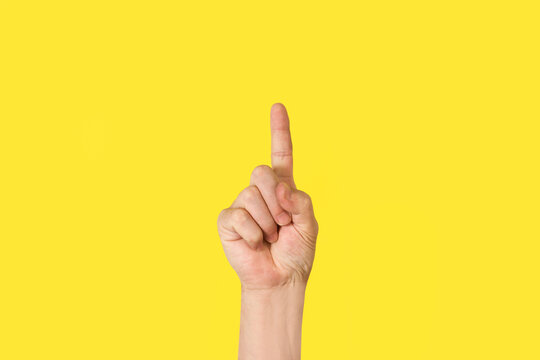 Mano de hombre apuntando con el dedo indice para arriba sobre un fondo amarillo brillante liso y aislado. Vista de frente y de cerca. Copy space