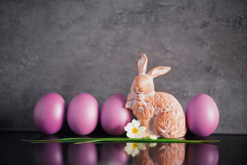 Easter decoration concept: ceramic easter bunny or rabbit with flower and pink colored eggs on dark grey stone background