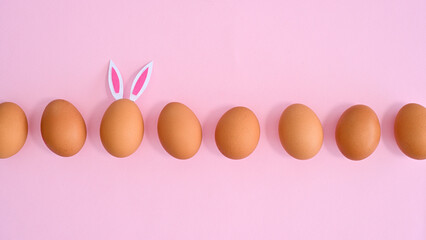 Easter pastel pink background with natural eggs and one different with bunny ears. Flat lay minimal. Spring holidays