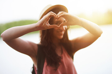 I heart the outdoors. Portrait of a happy young woman making a heart shape with her hands while exploring outdoors.