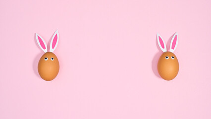 Two natural eggs with bunny ears and eyes on pastel pink background. Flat lay copy space Easter concept