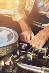 Making a few minor adjustments. Shot of a senior man looking under the hood of his car while on a roadtrip.