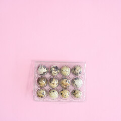 Plastic box and quail natural eggs in it on pastel pink background. Flat lay Easter concept