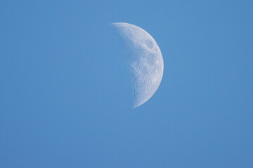 close up of the crescent moon in the daytime with blue sky