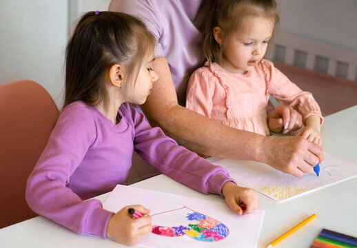 Grandma and her children draw a drawing with a felt-tip pen on paper with clouds and the sun. A woman teaches girls to draw. Kids carefully watch how grandmother draws.