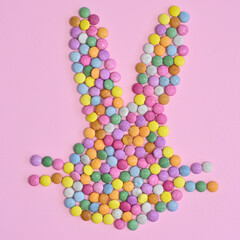 Creative rabbit bunny head made with colorful candies on pastel pink background. Flat lay Easter concept
