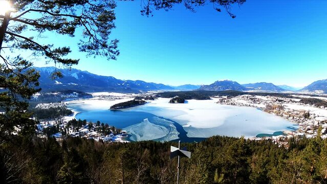 Panoramic view from a small hill in winter on Faak lake in Austrian Alps. Picturesque lake is surrounded by high mountains. The mountains are reflecting in calm surface of the lake. Taborhoehe, Tabor
