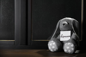 Toy bunny and card with word Depression near window on rainy night, space for text