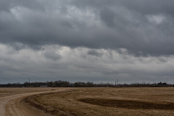 Fototapeta premium Stormy cloudy sky over an agricultural field with a dirt road in early spring.