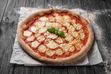 Delicious freshly baked Margherita pizza. Appetizing whole grain pizza with cheese and tomatoes. Traditional Italian pizza. Served on parchment paper. Dark wooden background with sprinkled with flour.