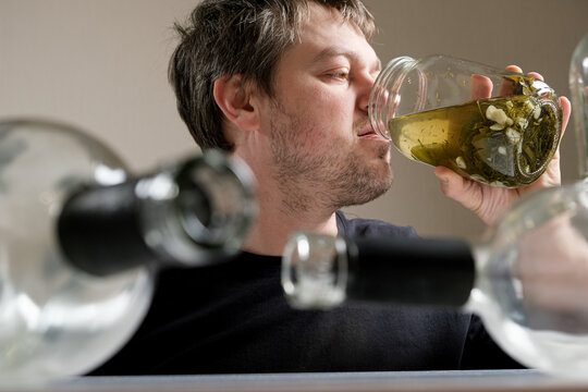 A man with alcohol dependence drinks brine from a jar of aole cucumbers, a man in a hangover.