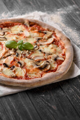 Freshly baked meat pizza. Appetizing pizza from whole grain dough with cheese, mushrooms and chicken meat. Served on parchment paper. Dark wooden background with sprinkled flour. Cropped image.