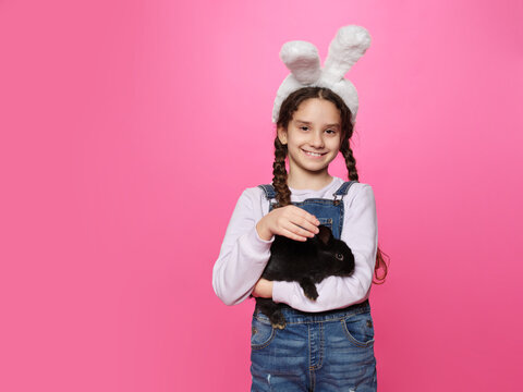 Cute Happy Girl With A Real Easter Bunny Wearing Ears Isolated Pink Background. Space For Text.