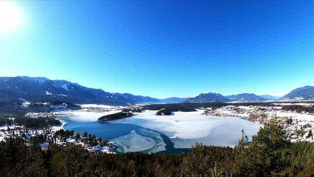 Panoramic view from a small hill in winter on Faak lake in Austrian Alps. Picturesque lake is surrounded by high mountains. The mountains are reflecting in calm surface of the lake. Taborhoehe, Tabor
