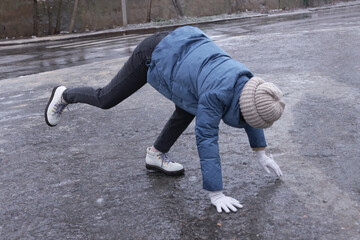 Young woman having difficulties with moving on icy road outdoors