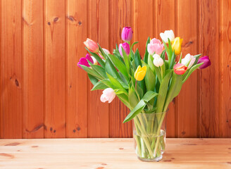 Bouquet of fresh colorful tulips in vase on wooden table.
