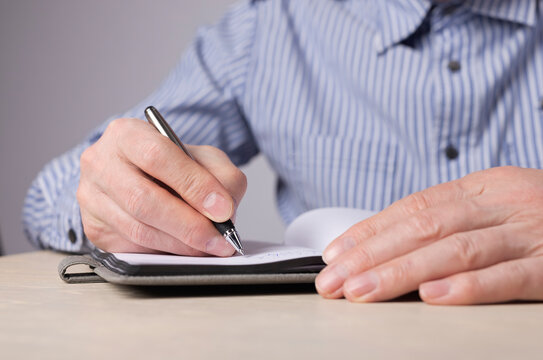 Man hands closeup taking notes in planner. Man sitting at desk in office or at home and writing with pen plans, agenda, thoughts, important information. High quality photo