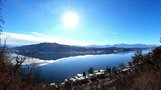 Panoramic view on the calm surface of the Woerthersee Lake in Carinthia, Austria. Lake is surrounded by high mountains. Small villages at the shores. View on Karawanks, Pyramidenkogel, Mittagskogel
