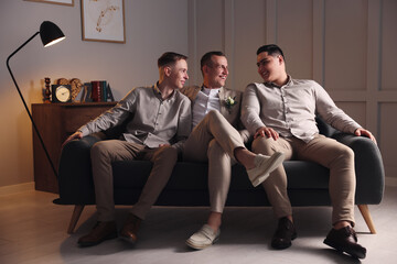 Happy groom and groomsmen sitting on sofa in room