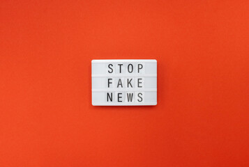 Stop fake news. The inscription on the lightbox on a red background. Flat lay, top view 