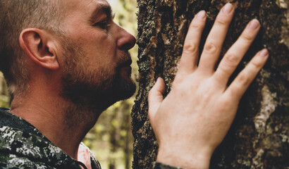 Adult man touches a huge tree, sniffs the bark and hugs the trunk. An adult man enjoys being alone...