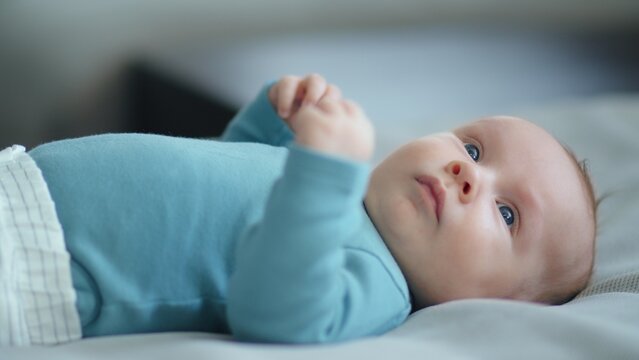 Sweet newborn boy lies on the sofa. Beautiful infant boy with blue eyes.  Cute two-month-old baby in blue clothes. Shooting from the lower angle of a chubby male kid.  Closeup portrait of calm baby.