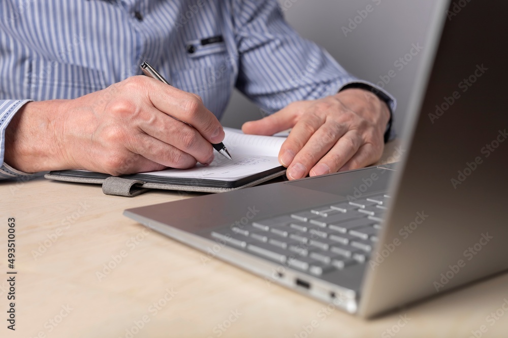 Poster man taking notes in planner and using laptop for online education, distant work. hands closeup. man 