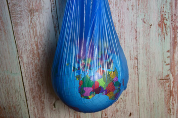 The globe of the planet Earth in a blue plastic trash bag on a background of wooden planks
