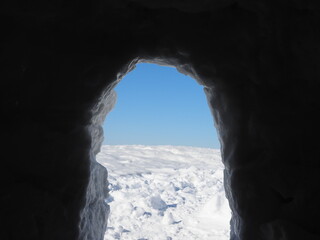 view from inside of a snow grotto into bright winter landscape in the austrian alps.