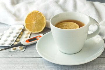 white cup with lemon tea on the background of a thermometer and pills in a blister. The concept of virus prevention and treatment.