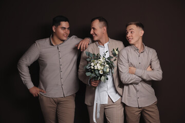 Happy groom with bouquet and his groomsmen on brown background - obrazy, fototapety, plakaty