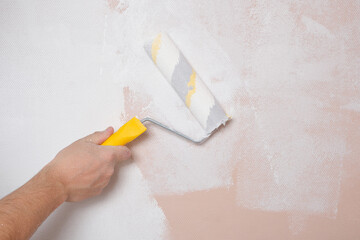 Painting the walls with a paint roller pink with white paint, home repairs.