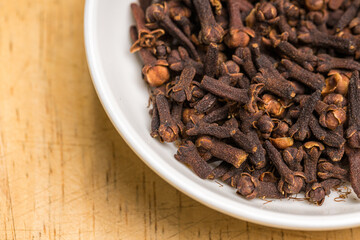 Cloves in a white bowl on wooden table
