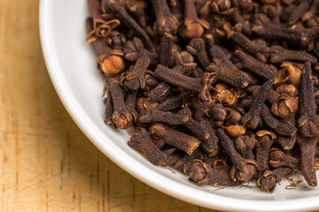 Cloves in a white bowl on wooden table