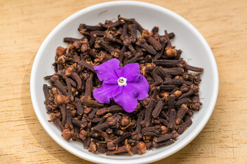 Cloves and pink flower in a white bowl on wooden table