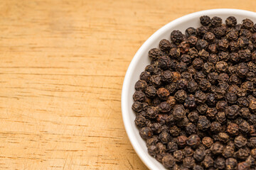 Black pepper in a white bowl on wooden table