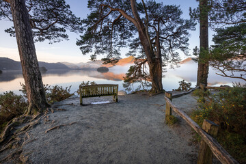 Lone wooden bench with peaceful view of misty lake on a fresh Winter morning. Friars Crag, Derwentwater, Lake District, UK.