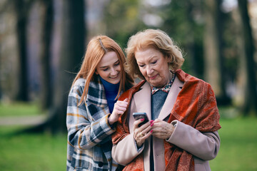 A granddaughter teaching her granny how to use mobile phone.