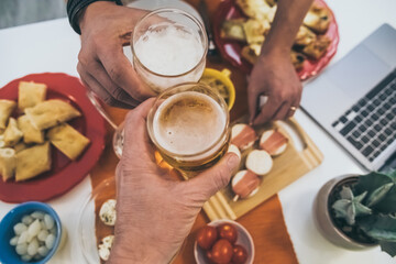 Toast with friend enjoying dinner together. Summer aperitif with group of friends. Joy and festivities in family View from the top of a table with many foods and glasses of beer in hands cheer up