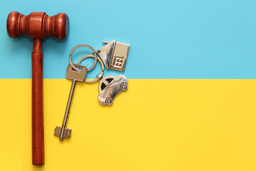 The key to the apartment with a keychain in the shape of a house and car on a cardboard blue yellow background, judge's gavel the colors of the flag of Ukraine.