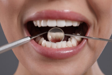 Examining woman's teeth with dentist's mirror on grey background, closeup