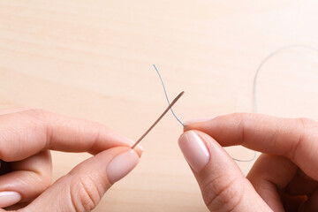 Woman threading sewing needle at table, closeup