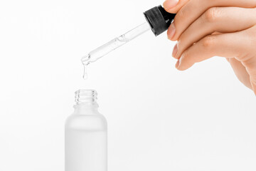 Woman hand holding pipette with collagen moisturizing hyaluron serum and drops the clear serum into the bottle. - obrazy, fototapety, plakaty