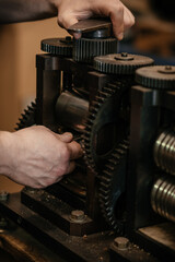 Close-up of gears of roll press. Rolling silver. Jewelry repair shop. Woman is out of focus in background.
