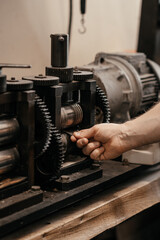 Close-up of gears of roll press. Rolling silver. Jewelry repair shop. Woman is out of focus in background.