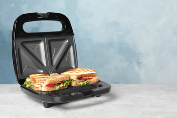Modern grill maker with sandwiches on grey table near light blue wall, space for text